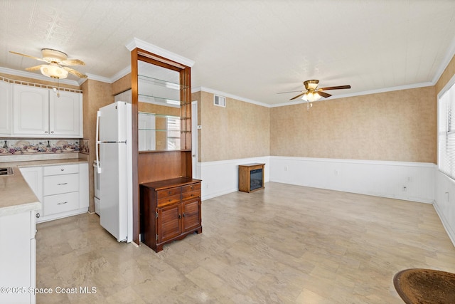 kitchen featuring ceiling fan, freestanding refrigerator, plenty of natural light, light countertops, and a wainscoted wall