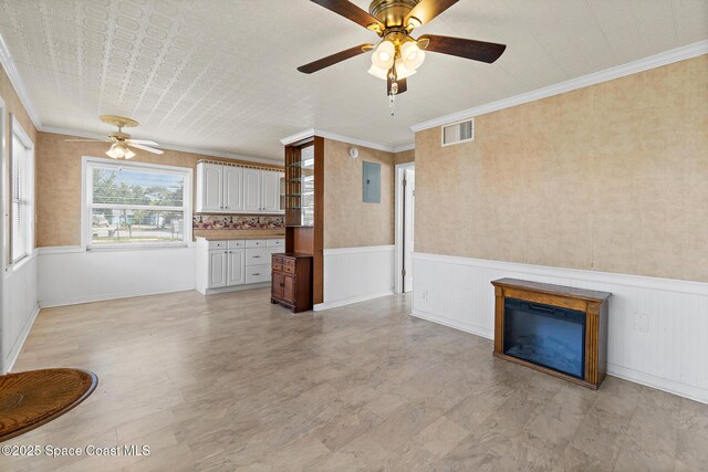 unfurnished living room with ceiling fan, wainscoting, ornamental molding, and electric panel