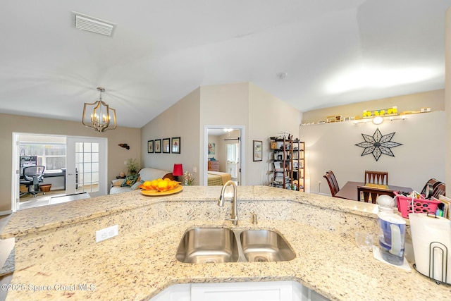 kitchen with lofted ceiling, sink, light stone counters, a notable chandelier, and decorative light fixtures