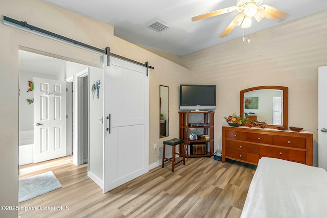 bedroom featuring a barn door, ceiling fan, and light wood-type flooring