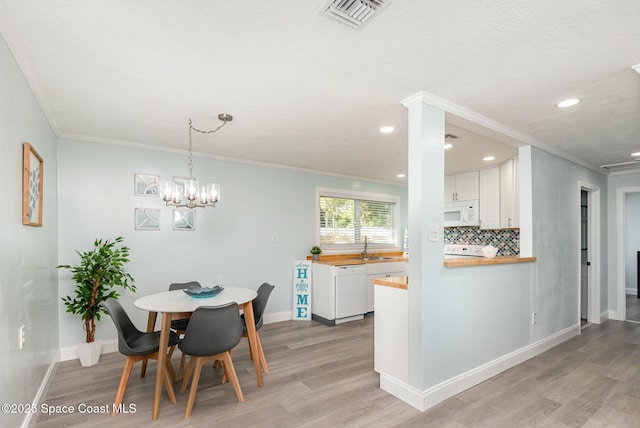 dining area featuring crown molding, sink, light hardwood / wood-style flooring, and a notable chandelier