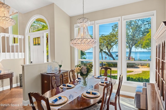 dining space with a water view, a healthy amount of sunlight, and a notable chandelier