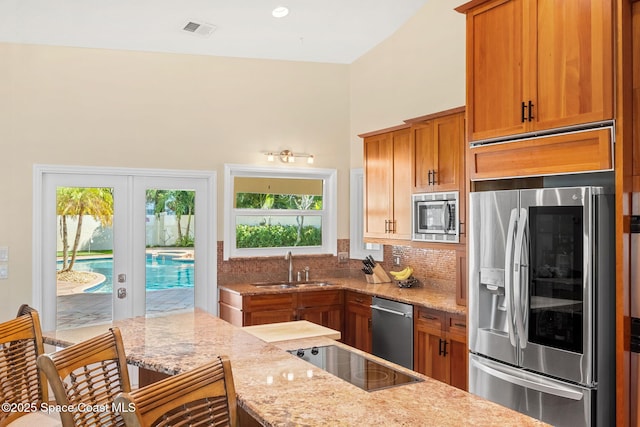 kitchen with sink, backsplash, stainless steel appliances, light stone countertops, and french doors