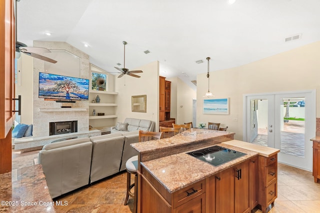 kitchen featuring a breakfast bar, decorative light fixtures, a kitchen island, black electric stovetop, and a fireplace