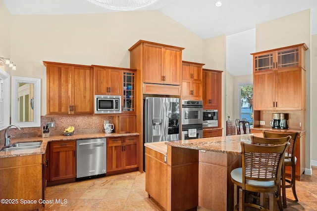 kitchen featuring sink, appliances with stainless steel finishes, tasteful backsplash, light stone countertops, and a kitchen island