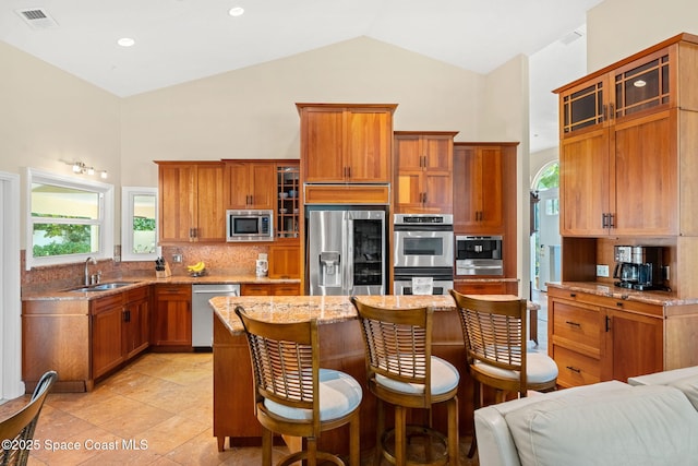 kitchen featuring sink, a center island, appliances with stainless steel finishes, light stone countertops, and backsplash