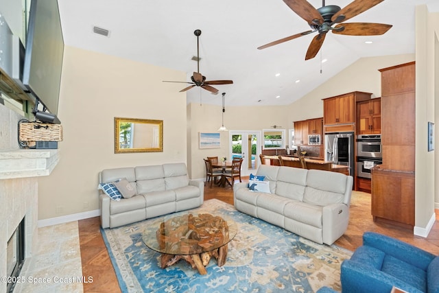 living room featuring ceiling fan, a tiled fireplace, and high vaulted ceiling