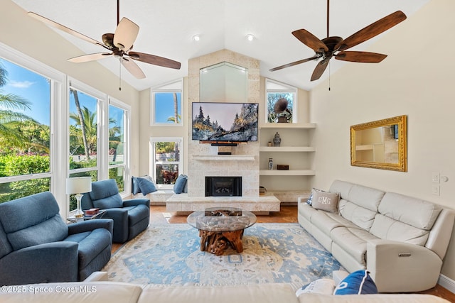 living room featuring ceiling fan, a stone fireplace, high vaulted ceiling, and built in features