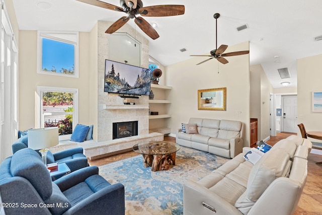 living room featuring ceiling fan, a large fireplace, built in shelves, and high vaulted ceiling