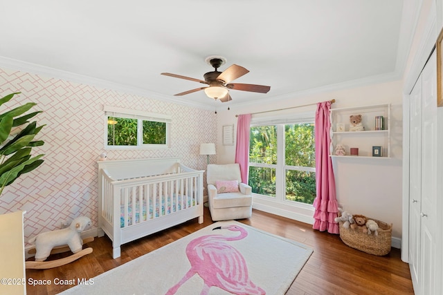 bedroom featuring a crib, ceiling fan, dark hardwood / wood-style floors, ornamental molding, and a closet