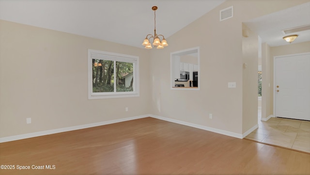 spare room featuring an inviting chandelier, vaulted ceiling, and light wood-type flooring