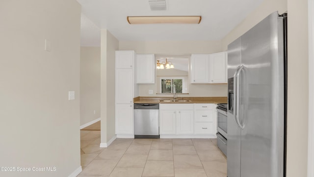 kitchen featuring sink, white cabinetry, stainless steel appliances, a notable chandelier, and light tile patterned flooring