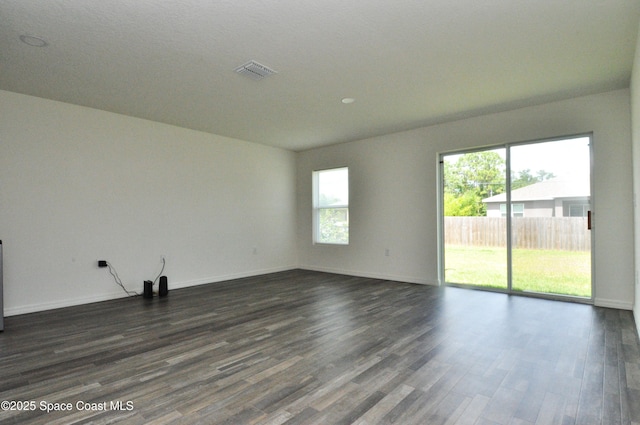 empty room featuring baseboards, dark wood-style floors, and visible vents