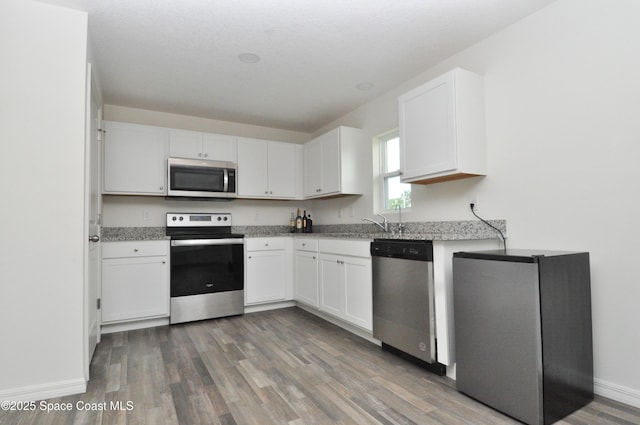 kitchen with baseboards, light stone countertops, wood finished floors, stainless steel appliances, and white cabinetry