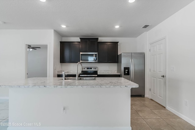 kitchen with a kitchen island with sink, sink, light tile patterned flooring, and appliances with stainless steel finishes