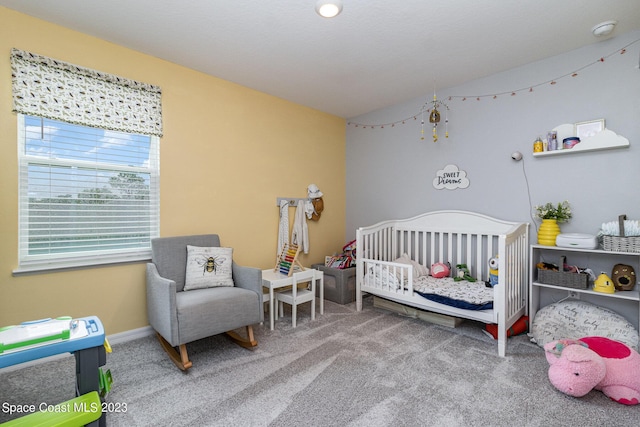 bedroom with a crib, lofted ceiling, and carpet flooring