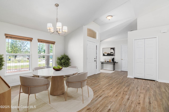 dining area with baseboards, light wood-type flooring, a notable chandelier, and vaulted ceiling