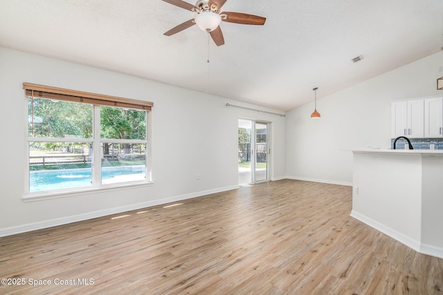 unfurnished living room featuring light wood finished floors, visible vents, vaulted ceiling, and ceiling fan