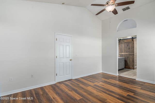 unfurnished bedroom with wood finished floors, baseboards, visible vents, and a barn door