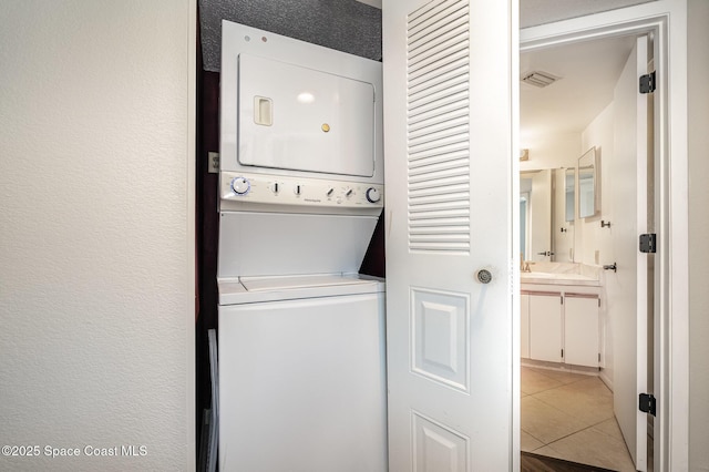 laundry area featuring stacked washer / drying machine and light tile patterned floors