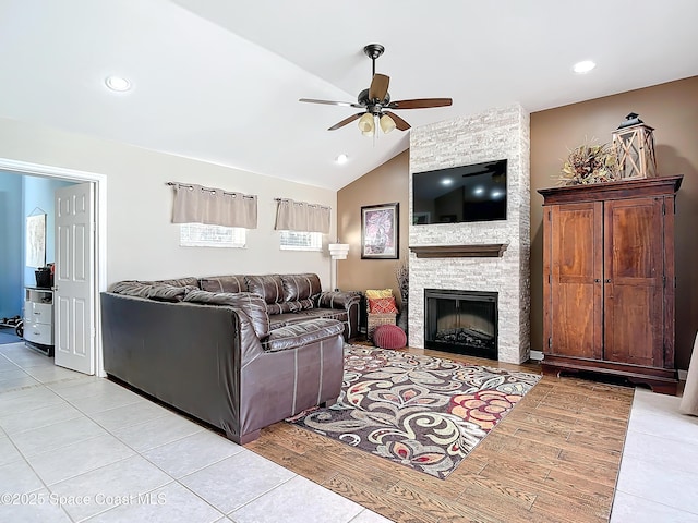 living room featuring ceiling fan, lofted ceiling, a fireplace, and light wood-type flooring