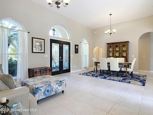 entryway with light tile patterned flooring, a towering ceiling, a notable chandelier, and french doors