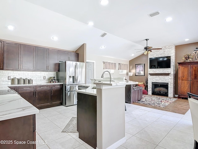 kitchen with lofted ceiling, stainless steel fridge, a kitchen island with sink, light tile patterned floors, and ceiling fan