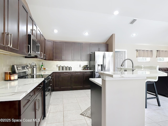 kitchen with light tile patterned flooring, appliances with stainless steel finishes, a kitchen breakfast bar, and a center island with sink