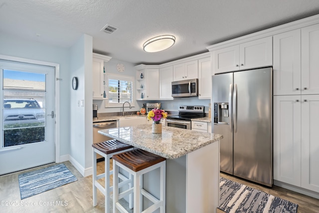 kitchen with white cabinetry, light stone counters, a kitchen island, and appliances with stainless steel finishes