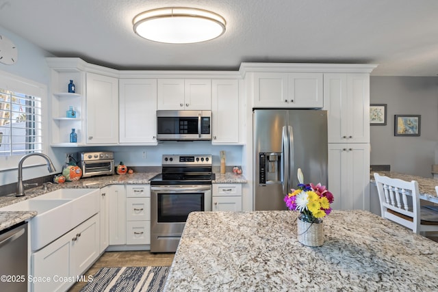 kitchen with light stone counters, sink, white cabinets, and appliances with stainless steel finishes