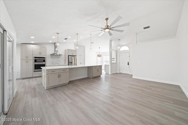 kitchen with gray cabinets, lofted ceiling, hanging light fixtures, a kitchen island with sink, and light wood-type flooring