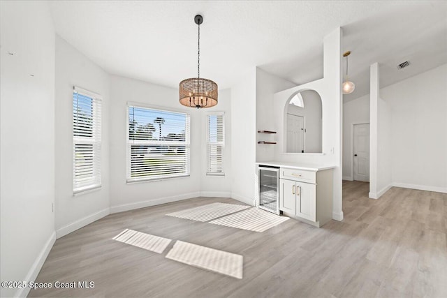 unfurnished dining area featuring beverage cooler, a chandelier, and light wood-type flooring