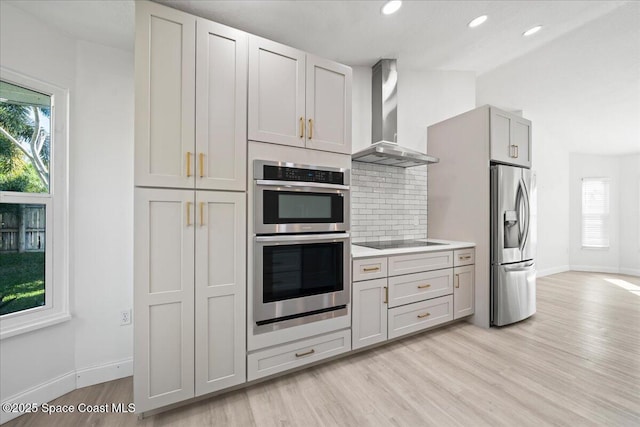 kitchen with wall chimney range hood, backsplash, stainless steel appliances, a wealth of natural light, and light wood-type flooring