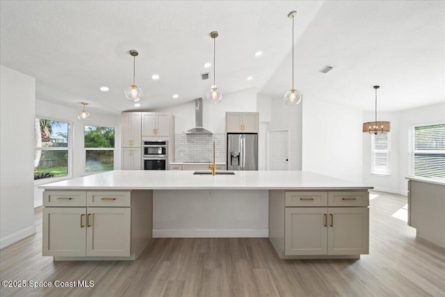 kitchen featuring a spacious island, appliances with stainless steel finishes, gray cabinets, and wall chimney range hood