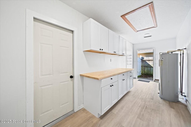 kitchen featuring light hardwood / wood-style floors, butcher block countertops, water heater, and white cabinets