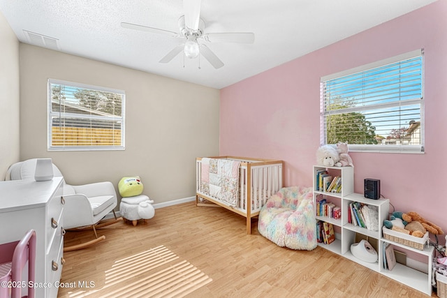 bedroom with hardwood / wood-style flooring, a nursery area, a textured ceiling, and ceiling fan