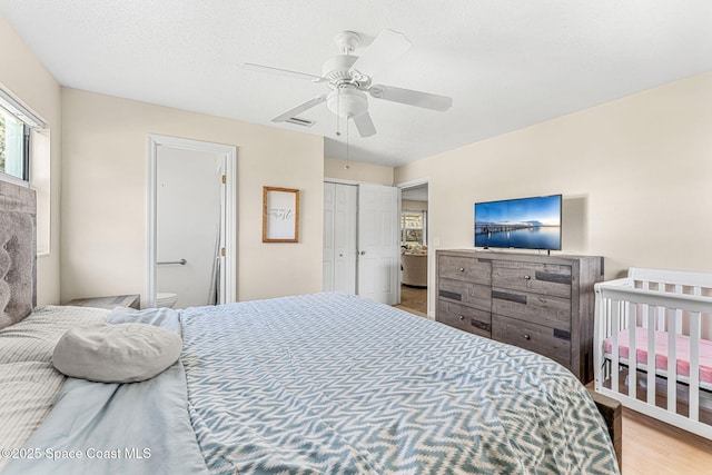 bedroom with ceiling fan, connected bathroom, light hardwood / wood-style floors, a textured ceiling, and a closet