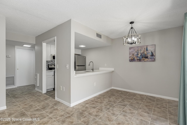 kitchen with sink, white cabinetry, an inviting chandelier, a textured ceiling, and stainless steel refrigerator