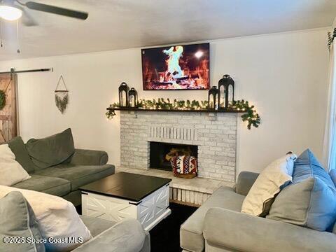 living room featuring a barn door, ceiling fan, and a brick fireplace