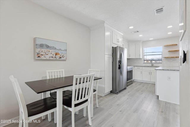 kitchen with sink, tasteful backsplash, light wood-type flooring, appliances with stainless steel finishes, and white cabinets