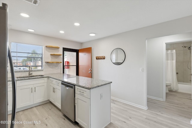 kitchen with sink, light stone counters, dishwasher, kitchen peninsula, and white cabinets