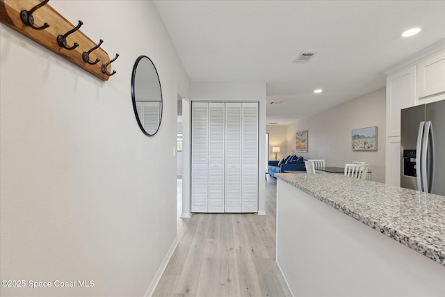 kitchen featuring white cabinetry, light stone countertops, light wood-type flooring, and stainless steel fridge with ice dispenser