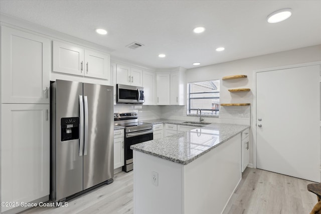 kitchen featuring sink, light stone counters, appliances with stainless steel finishes, kitchen peninsula, and white cabinets