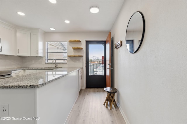 kitchen featuring sink, tasteful backsplash, light stone countertops, white cabinets, and kitchen peninsula