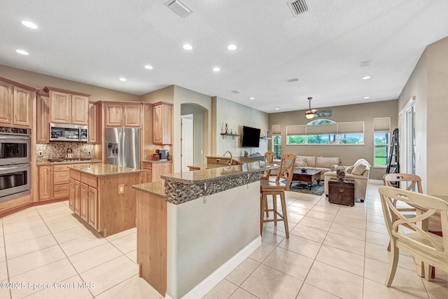 kitchen featuring light tile patterned flooring, appliances with stainless steel finishes, backsplash, a kitchen bar, and a center island