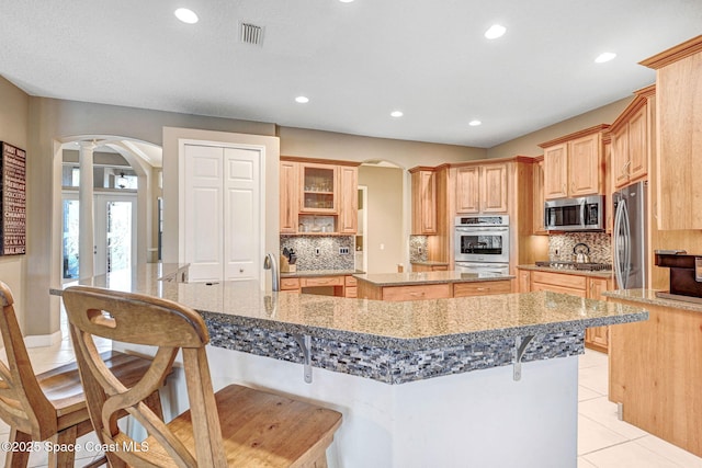 kitchen featuring stainless steel appliances, stone countertops, a kitchen island with sink, and a kitchen breakfast bar