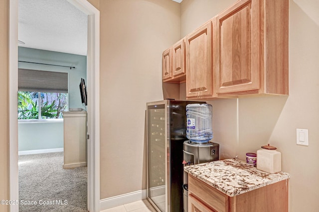 kitchen with light brown cabinetry, light carpet, light stone countertops, and a textured ceiling