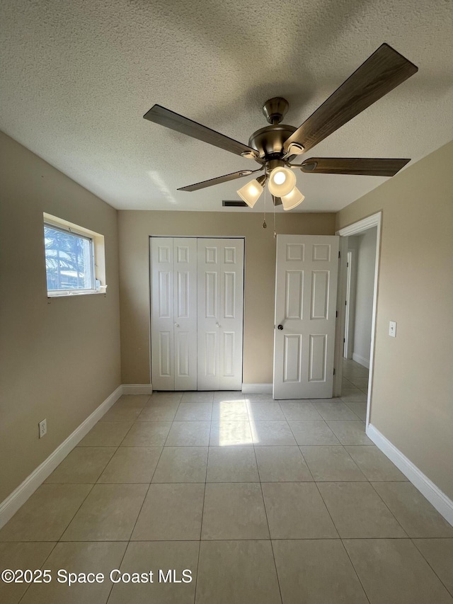 unfurnished bedroom featuring light tile patterned flooring, ceiling fan, a closet, and a textured ceiling