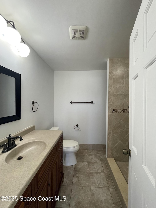 bathroom with tiled shower, vanity, toilet, and tile patterned floors