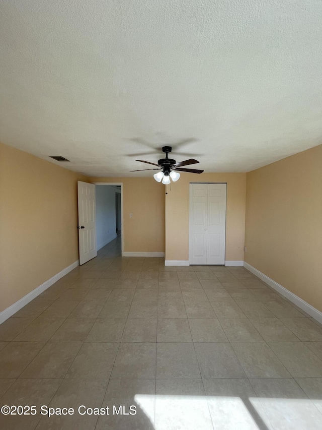 empty room with ceiling fan, a textured ceiling, and light tile patterned floors